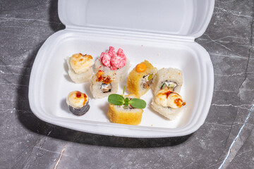 A styrofoam container with assorted sushi rolls, including tempura-fried and baked variations,...