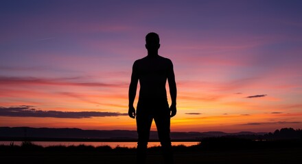 A silhouetted figure stands by a calm body of water, admiring a breathtaking sunset. The sky glows with vibrant orange, pink, and purple hues, evoking tranquility and introspection.