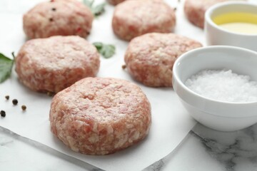 Many uncooked patties and spices on white marble table, closeup