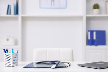 Laptop, stethoscope and folders on desk in medical office, closeup