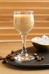 Coffee cream liqueur in glass, ice and beans on wooden table, closeup