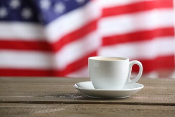 Aromatic coffee in cup on wooden table against flag of USA, space for text