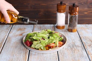 Woman pouring oil onto tasty salad at color wooden table, closeup
