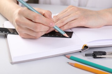 Woman drawing sketch with ruler and pencil on notebook at white table, closeup