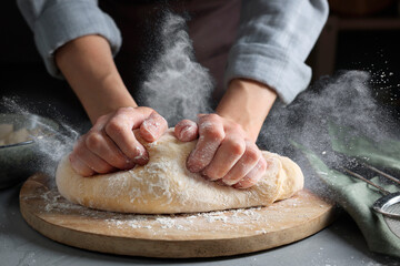 Woman kneading dough at grey table, closeup. Cloud of flour