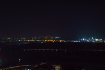 Aerial view of Abu Dhabi at night, showcasing the city's illuminated skyline, modern skyscrapers, and roads glowing under the night sky.