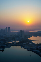 Aerial view of Abu Dhabi in the morning light, as the rising sun casts a golden glow over the city's modern skyline.