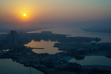Aerial view of Abu Dhabi in the morning light, as the rising sun casts a golden glow over the city's modern skyline.