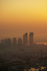 Aerial view of Abu Dhabi in the morning light, as the rising sun casts a golden glow over the city's modern skyline.