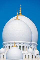 Close-up of the Sheikh Zayed Grand Mosque, showcasing its intricate white marble domes and elegant architectural details against a vivid blue sky. 