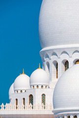 Close-up of the Sheikh Zayed Grand Mosque, showcasing its intricate white marble domes and elegant architectural details against a vivid blue sky. 