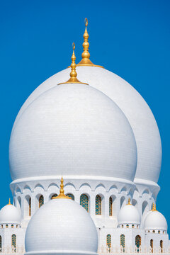 Close-up of the Sheikh Zayed Grand Mosque, showcasing its intricate white marble domes and elegant architectural details against a vivid blue sky. 