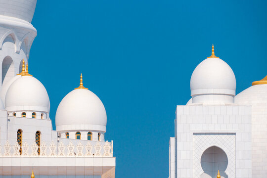Close-up of the Sheikh Zayed Grand Mosque, showcasing its intricate white marble domes and elegant architectural details against a vivid blue sky. 