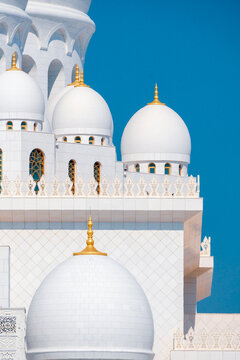 Close-up of the Sheikh Zayed Grand Mosque, showcasing its intricate white marble domes and elegant architectural details against a vivid blue sky. 