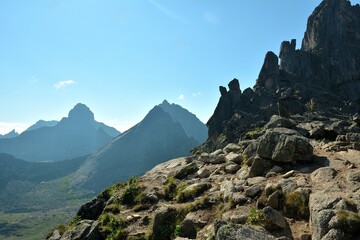 View from the edge of a rocky mountain slope onto a picturesque valley with high pointed rocks on a sunny lazy morning.