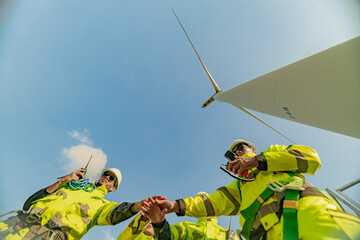 A team of engineers celebrates success after completing wind turbine maintenance at a wind farm....