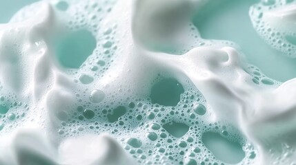 A close-up macro photograph of thick, creamy white soap suds with intricate bubble patterns, set against a soft light green background