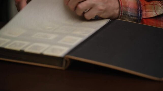 stamp collector checks his collection and enjoys it in blurry way. male hands open and flip through blurred pages postage stamp collection album. close-up.