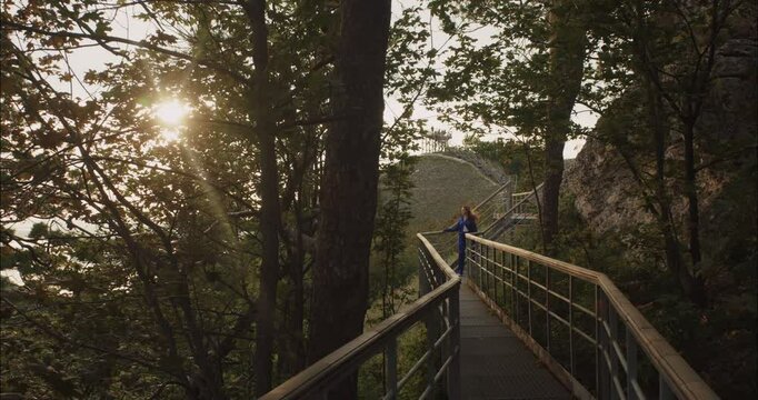 Young woman walking on a scenic mountain footbridge at sunset