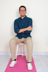 Full body portrait of a man sitting on the bench smiling happy with arms crossed
