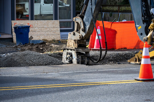 Roadworks covering trench dug for underground utilities with gravel and compacting with vibrating tamper attachment on excavator machine, new housing development construction project
