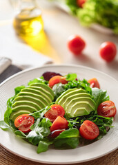 Fresh Mixed Green Salad with Avocado, Tomatoes, and Olive Oil in Natural Light on White Plate