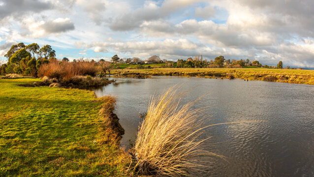 Tranquil riverbank of the South Esk River in Tasmania, lined with grasses and surrounded by open pastureland or farmland, showcases a serene rural riverside environment in regional Australia
