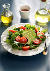 Fresh Mixed Green Salad with Avocado, Tomatoes, and Olive Oil in Natural Light on White Plate