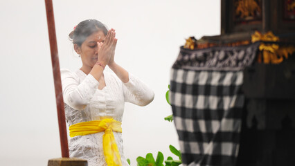 Young balinese woman praying at a traditional temple in Bali, incense, tradition and culture