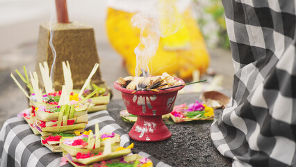 Balinese offering, known as canang sari, in bali ceremony at temple, praying woman in background, incense burning