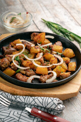 Fried potatoes with meat and onions in a frying pan. Served on a wooden board on the table, close up