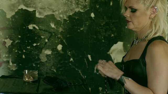 Woman punk musician wraps the strap of her black leather gloves around her wrist. She is extinguishing a cigarette in an ashtray. Female artist getting ready for her performance