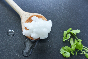 A wooden spoon with coconut oil in a pan, close-up.