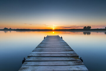 Obraz premium Scenic wooden pier extending into a tranquil lake at sunset with golden reflections