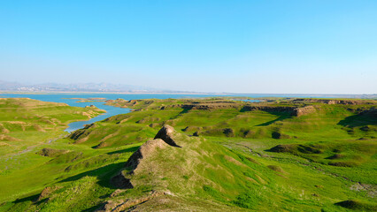 A vast landscape of green hills, a winding river, and distant mountains beneath a bright blue sky.