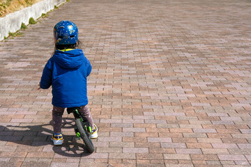 Child in Blue Jacket Riding a Bike on a Paved Surface