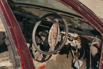 A close-up view of a stripped-down car interior, featuring a rusted steering wheel and exposed mechanical parts in a deteriorated state.