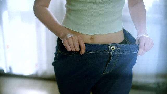 Woman demonstrates weight loss with oversized jeans in well-lit room 