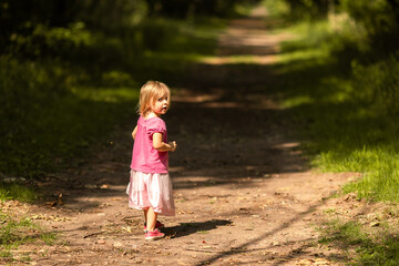 A young girl pauses on a sunlit forest path, looking back curiously