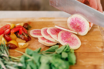 Slicing fresh watermelon radish and heirloom tomatoes on a woode
