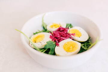 A fresh salad bowl with boiled eggs, arugula, and pickled cabbag