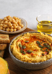close up Homemade pumpkin chickpea hummus in a bowl on wooden board on light background. copy space