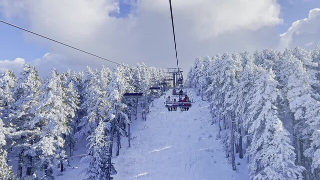 Chairlift in beautiful snowy mountains in a ski resort. Skiers on the ski lift, white snow pine trees
