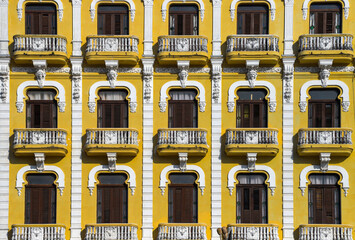 This image features a vibrant yellow building facade adorned with ornate white architectural details, including decorative balconies, intricate carvings, and symmetrically framed windows.cuba .havana