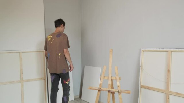 The artist puts the canvas on the easel. Minimalist light studio for painting.