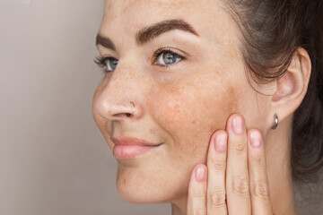 Portrait of cropped caucasian middle aged woman face with freckles touching skin by hand. Age spots on the face. Woman with blue eyes