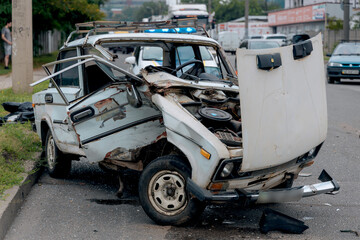 The aftermath of a traffic accident on a city road, close-up. A car with a broken front end and an open hood is at the scene of the accident. Broken windshield.