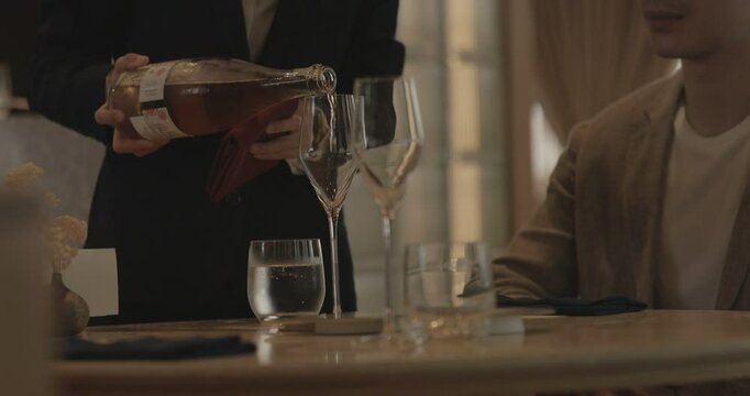 Pouring wine into a wine glass for a guest in fine dining restaurant. Warm ambience. Wine pouring by waitress. Luxury dining environment. Food and beverage service industry.