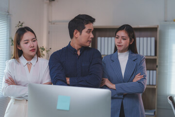 Obraz premium Three asian businesspeople standing with arms crossed, intently discussing work issues while analyzing a desktop computer in a corporate office setting