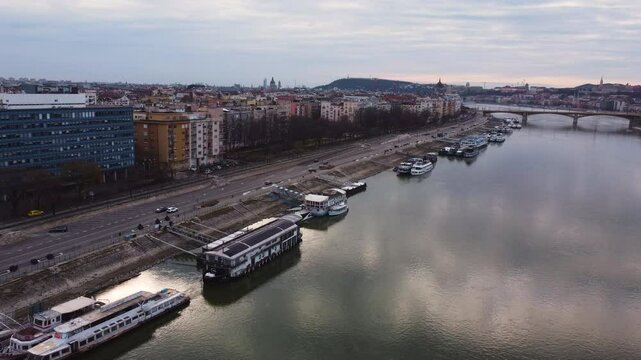 Aerial establishing Danube River in Budapest, city buildings lining waterfront on both sides with ferries in water near reformed church on Pozsonyi Street, Margitsziget or margit hid bridge